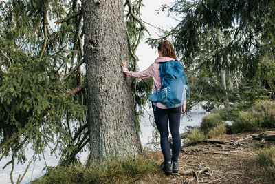 A young woman traveler with a backpack on her back enjoys the views in the spring forest. hiking