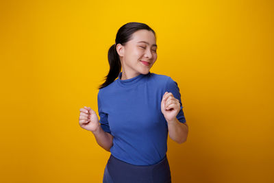 Smiling young woman standing against yellow background