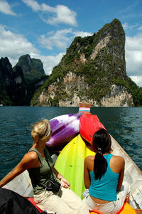 Women sitting on boat in lake against mountains