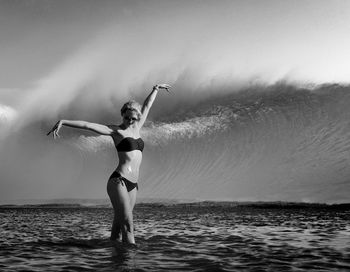 Woman in bikini standing in sea against sky