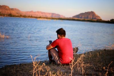 Rear view of man sitting on lakeshore