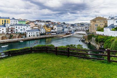 Buildings by river against cloudy sky