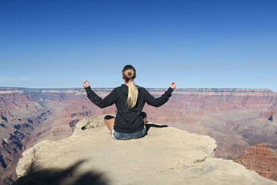 Rear view of woman meditating at grand canyon against blue sky