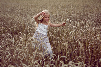 Blonde girl walks through dry wheat in summer field