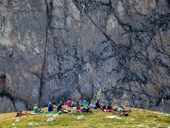 People sitting on grassy field against mountain