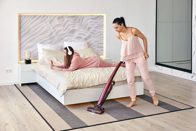 Daughter lying in bed while mother cleaning floor