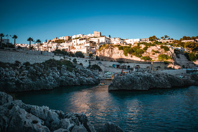 Buildings by sea against clear blue sky