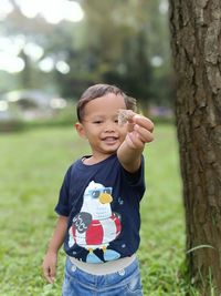 Portrait of boy standing against tree and catching a butterflies
