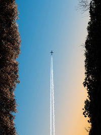 Low angle view of a plane with smoke trails against clear sunset sky