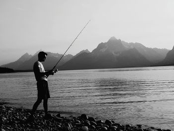 Man fishing in lake against mountains