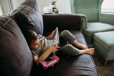 Young boy sitting on couch playing educational game on tablet