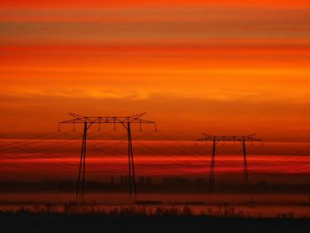 Silhouette electricity pylon against orange sky