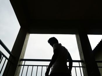 Low angle view of silhouette man standing by railing against sky