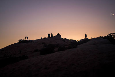 Silhouette people standing on rock against sky during sunset