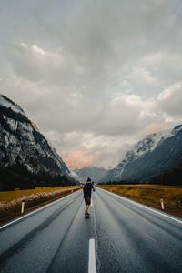 Rear view of man on road against cloudy sky