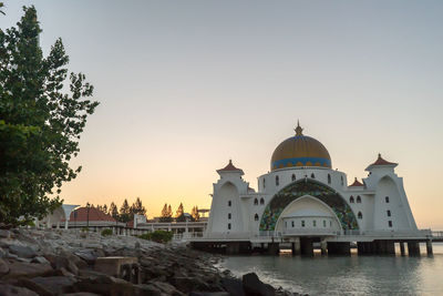 Mosque over sea against sky during sunset