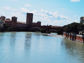 Arch bridge over river by buildings against sky