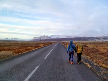 Rear view of people standing on road against sky