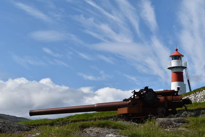 Cannon near lighthouse against cloudy sky
