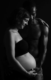 Midsection of shirtless woman against black background