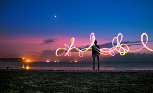 Woman standing on illuminated beach against sky at night