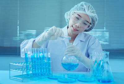 Young female scientist pouring chemical in flask at laboratory