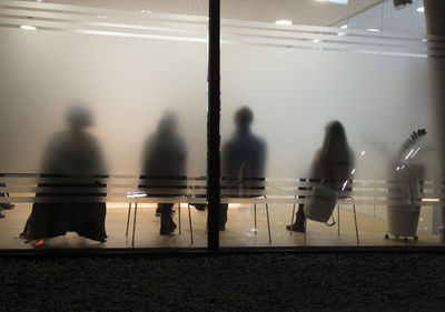 Rear view of people sitting in office seen from frosted glass wall