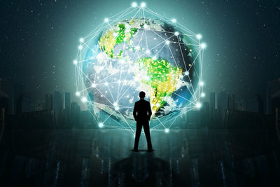 Digital composite image of silhouette businessman standing against illuminated globe at night