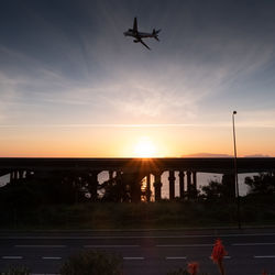 Silhouette airplane flying against sky during sunset
