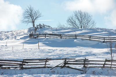 Fencing on snow covered field against sky