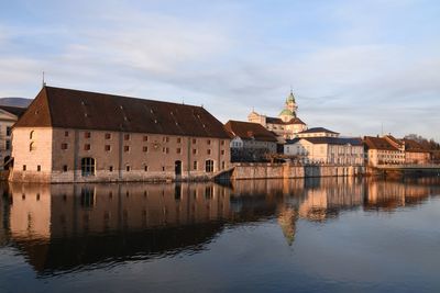 Buildings by river against sky in city