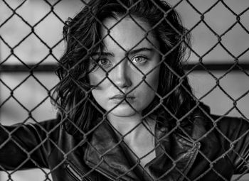 Portrait of young woman seen through chainlink fence