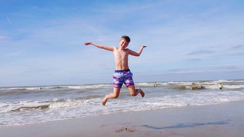 Full length of shirtless man at beach against sky