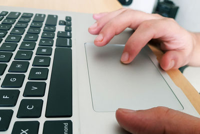 Cropped hands of person using laptop on wooden table