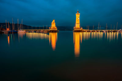 Illuminated buildings by sea against sky at night