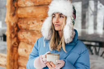 Portrait of a caucasian woman in a winter hat with earflaps with a mug of hot drink.