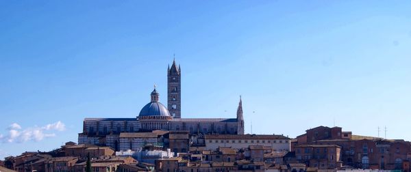 Buildings and duomo di siena against blue sky