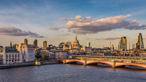 Bridge over river in city against cloudy sky