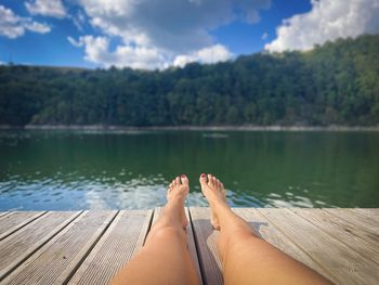 Woman with her tanned legs resting on a wooden pontoon near a lake surrounded by forest