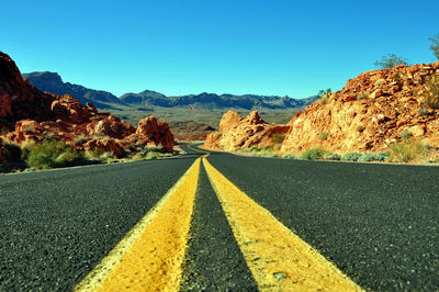 Empty road leading towards mountains against blue sky