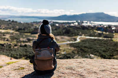 Rear view of woman sitting on mountain against sky