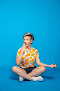 Low angle view of boy sitting against blue background