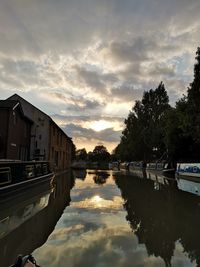 Scenic view of lake by buildings against sky during sunset