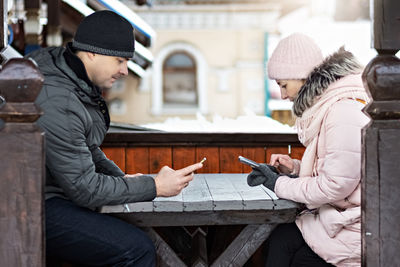 A couple is waiting for their order for lunch in a street cafe, texting by phone. communication