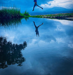 Man jumping in lake against sky