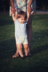 Baby boy with blonde hair and blue eyes on grass making first steps in mom arms