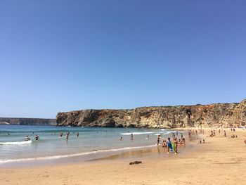 People on beach against clear blue sky