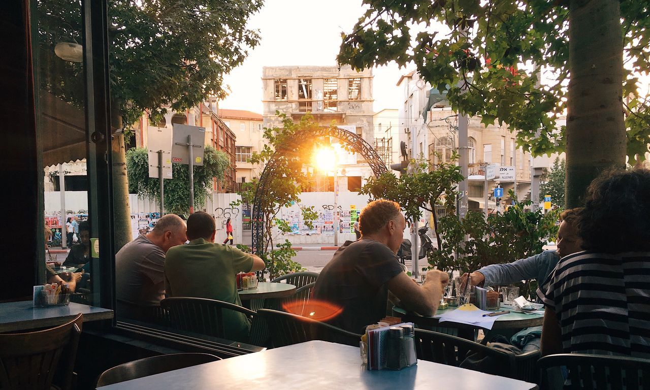 built structure, tree, building exterior, architecture, real people, city, large group of people, city life, men, women, street, restaurant, cafe, sidewalk cafe, sitting, lifestyles, outdoors, day, group of people, sky, people