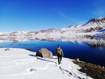 Rear view of man standing on snowcapped mountain against clear blue sky