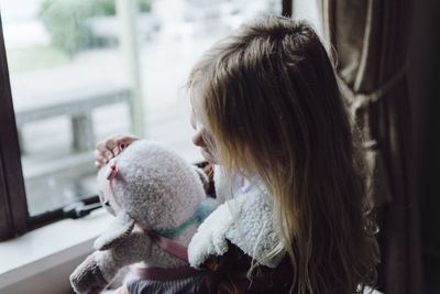 High angle view of girl holding stuffed toy against window